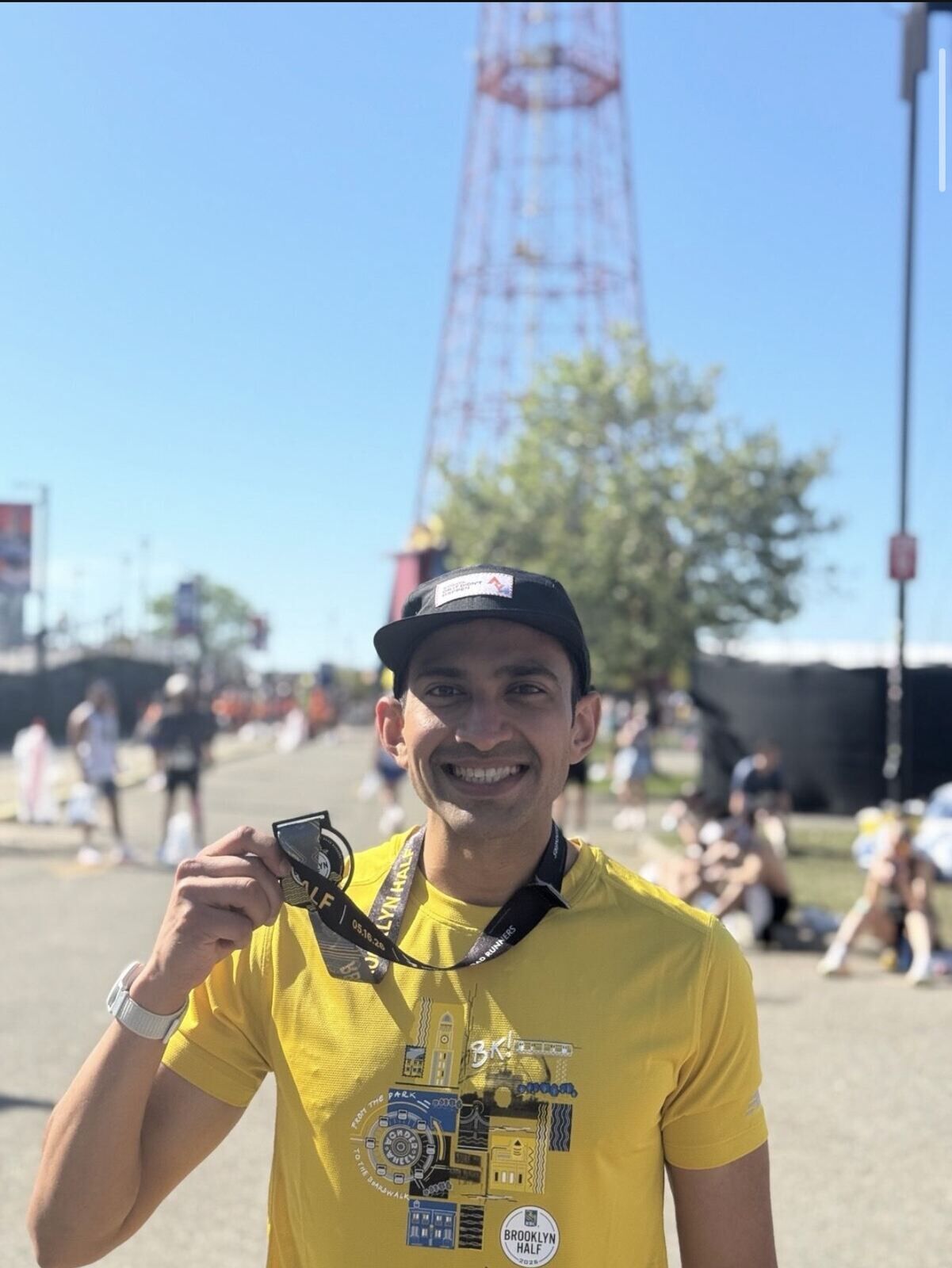 Harsh smiling and holding a Brooklyn Half 2026 finisher medal in front of the Coney Island Parachute Jump